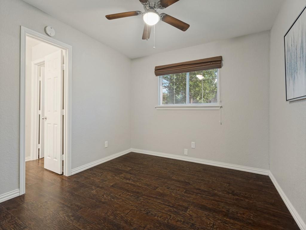 Room featuring wood-finish flooring, a ceiling fan with integrated lighting, a sliding window with a roller shade, and a six-panel door