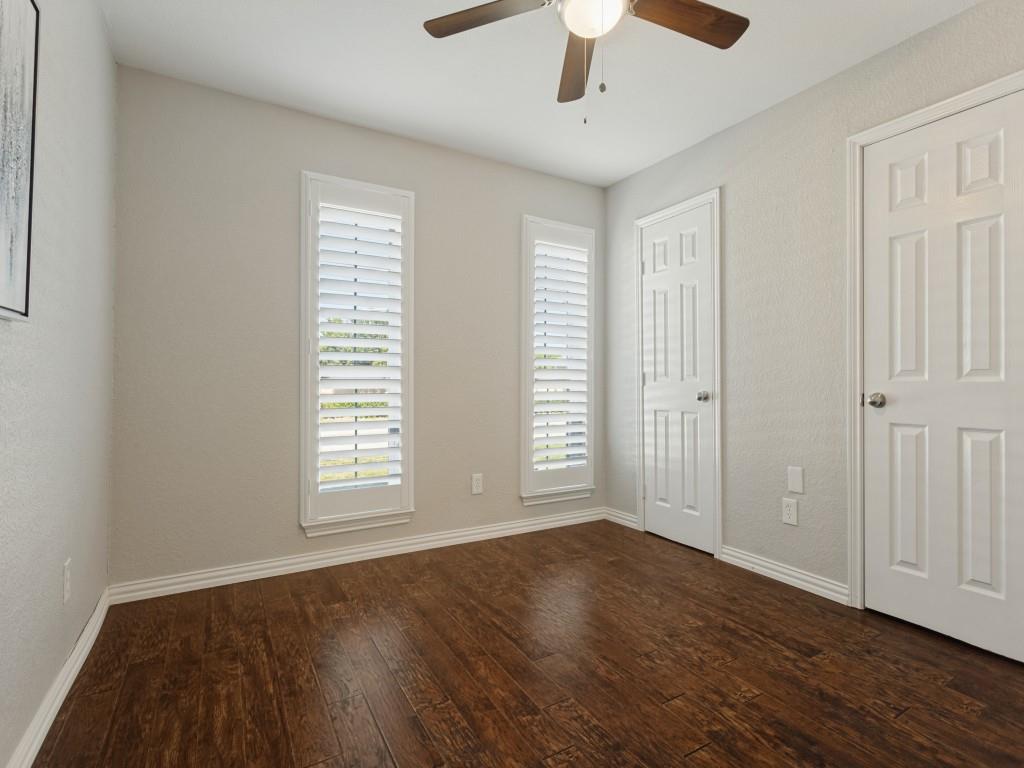 Wood-finish flooring, white plantation shutters, neutral wall color, and a ceiling-mounted light fixture with a fan