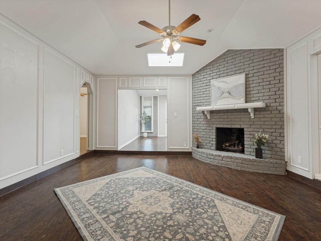 Vaulted ceiling with a skylight, wood-finish flooring, floor-to-ceiling wainscoting, and a painted brick fireplace with a decorative mantel