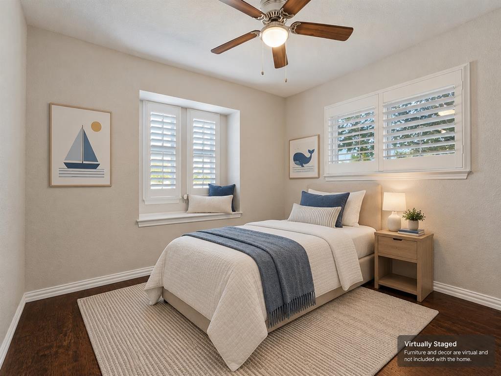 Bedroom featuring wood-finish flooring, recessed window nook, white plantation shutters, and a ceiling fan with integrated lighting