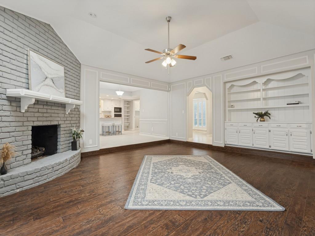 Vaulted ceilings, wood-finish flooring, painted brick fireplace with a decorative mantel, and built-in floor-to-ceiling cabinetry with millwork detailing