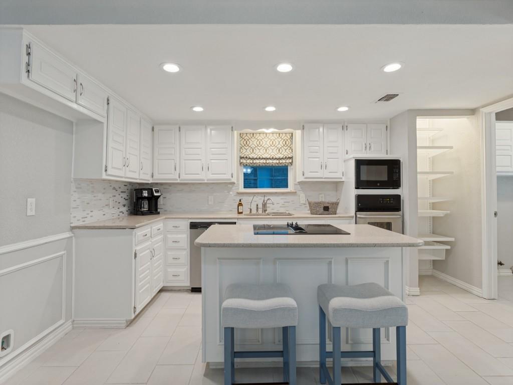 Kitchen featuring white cabinetry, center island with cooktop, neutral stone-composite countertops, tile flooring, and integrated wall oven and microwave