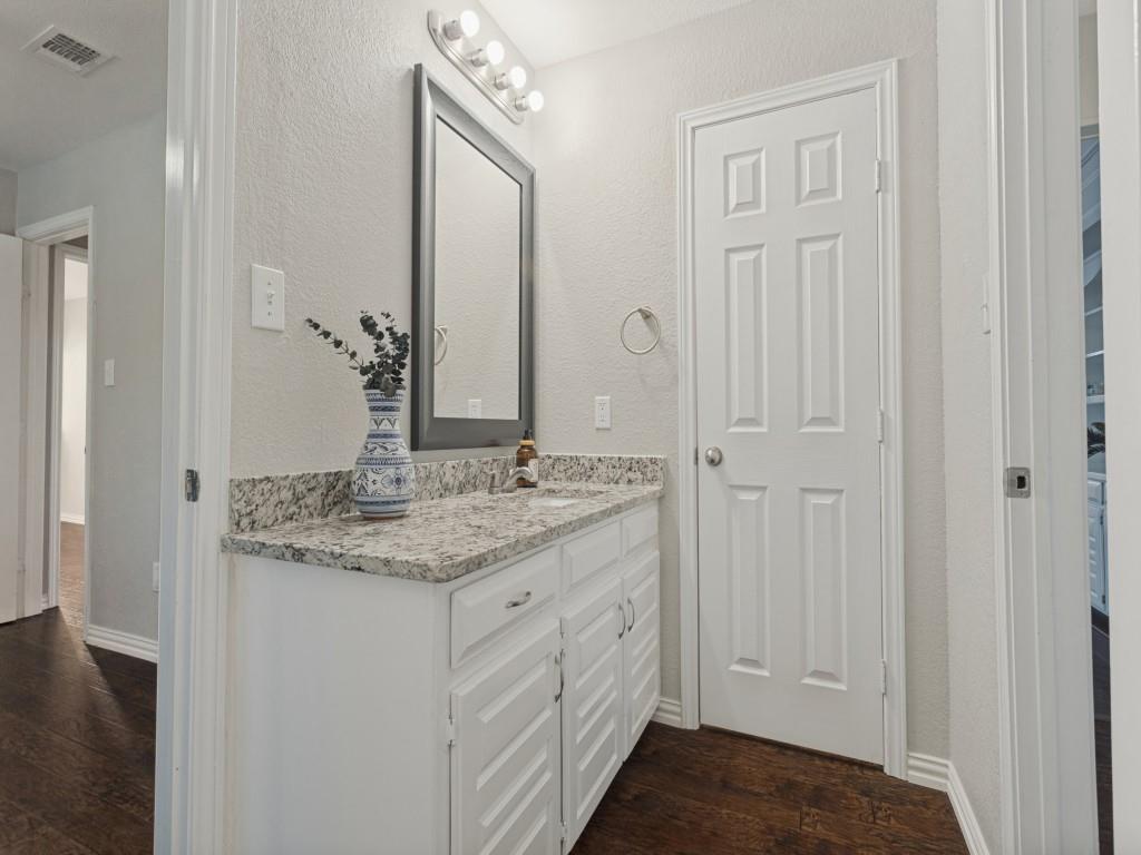 White vanity cabinet with a stone countertop, integrated sink, framed mirror, and multi-bulb vanity light fixture