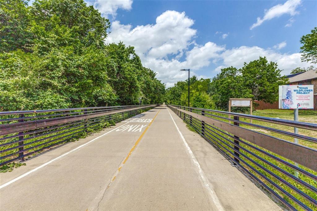 Paved multi-use trail featuring metal guardrails and mature tree canopy