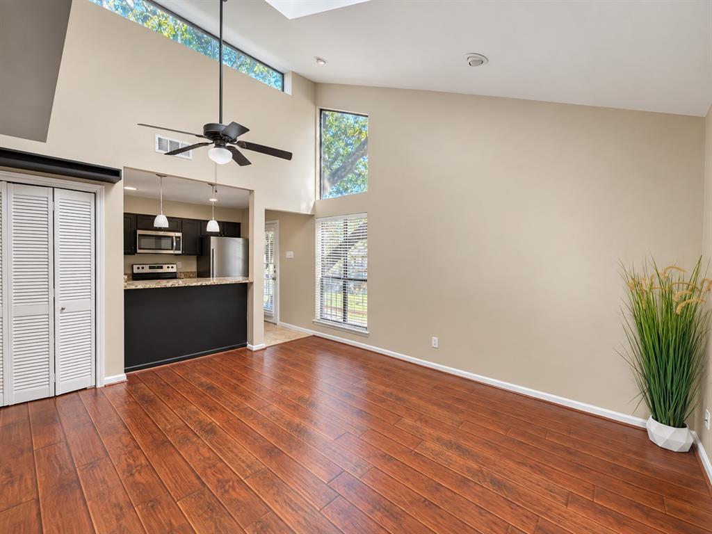 Vaulted ceiling with clerestory windows, wood-finish flooring, and recessed kitchen area featuring stainless steel appliances and stone-surface breakfast bar