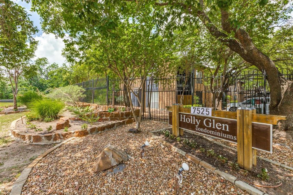 Exterior signage featuring wood-post construction, stone-retaining walls, gravel landscaping, and mature trees