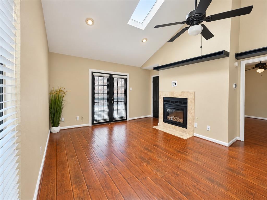 Vaulted ceiling featuring a skylight, wood-finish flooring, fireplace with a tiled surround, and black-framed French doors