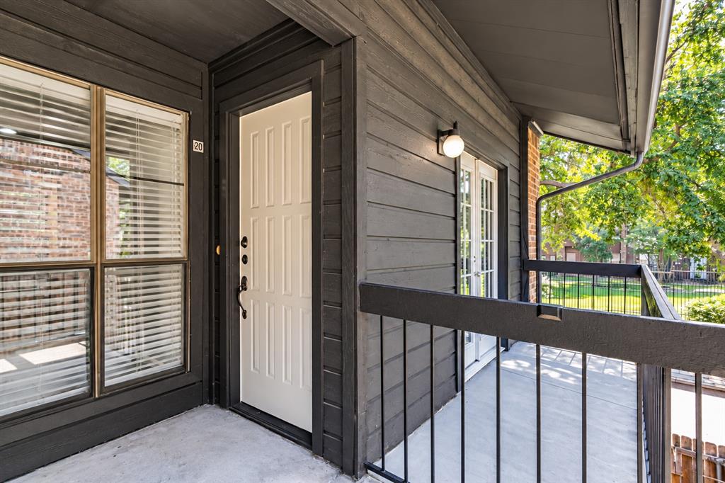 Covered balcony featuring dark horizontal wood siding, a paneled door, black metal railings, and an exterior wall-mounted light fixture