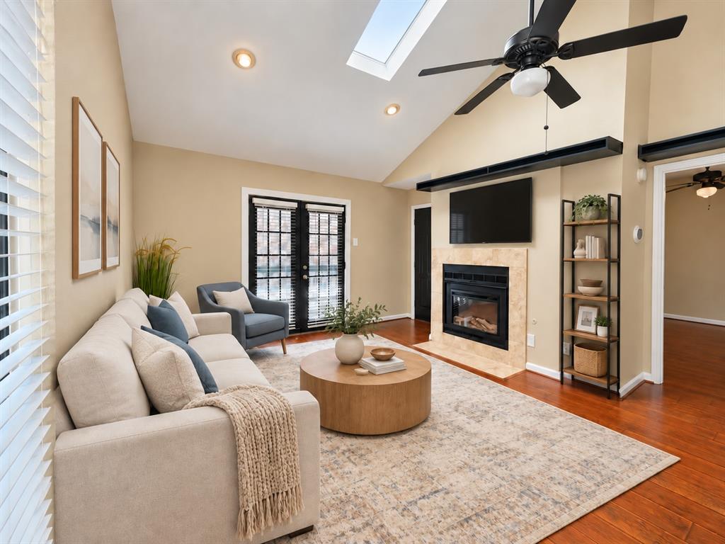 Vaulted ceiling with a skylight, fireplace with a tiled surround, wood-finish flooring, and black-framed French doors
