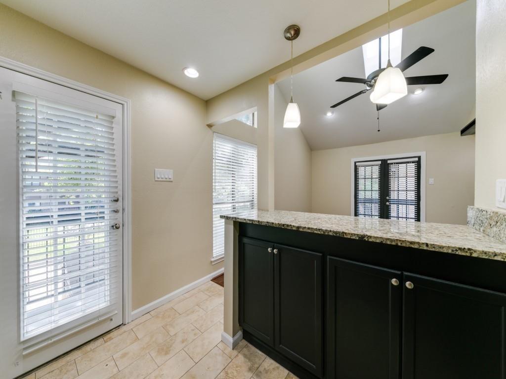 Kitchen features dark-finish cabinetry, stone-patterned countertops, tile flooring, dual pendant lighting, and a vaulted ceiling with a mounted ceiling fan