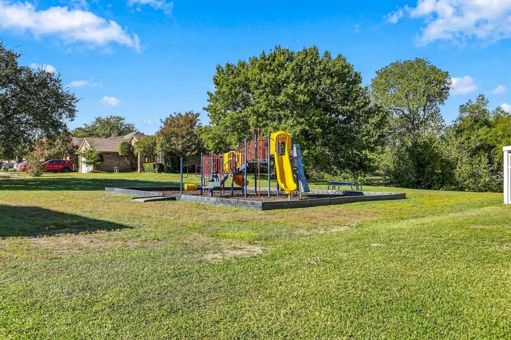 Expansive backyard featuring a dedicated playground structure, mulch-lined recreation area, mature trees, and open green space