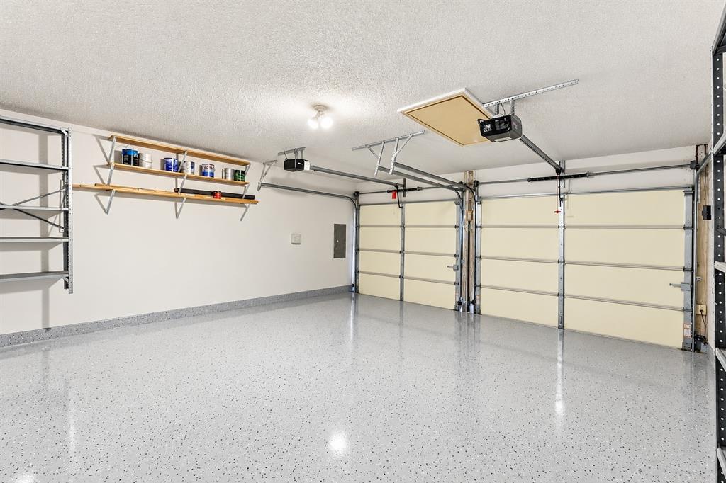 Two-car garage featuring epoxy-coated flooring, built-in wall shelving, an automatic door opener system, and attic access