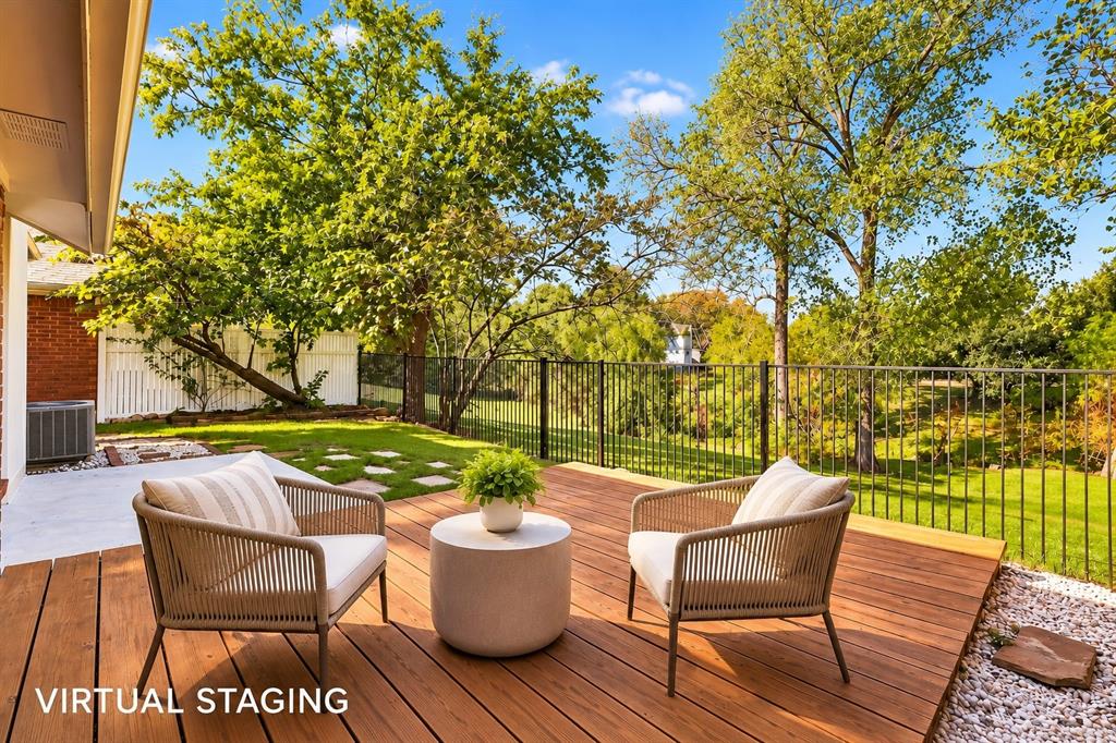 Rear wood-plank deck featuring a black metal perimeter fence, concrete patio area, and mature perimeter trees