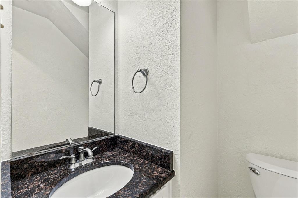 Dark stone-finish countertop with an integrated oval under-mount sink, chrome dual-handle faucet, large wall-mounted mirror, and circular chrome towel ring