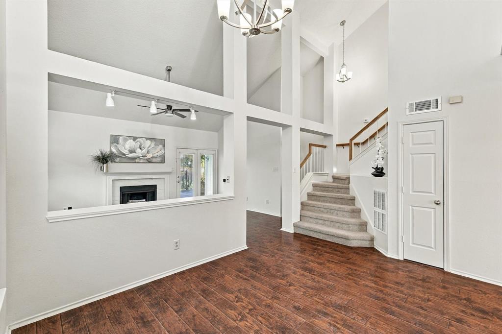 Vaulted ceilings featuring multi-tiered architectural cutouts, wood-finish flooring, a built-in fireplace with a mantel, and a carpeted staircase with a wood handrail
