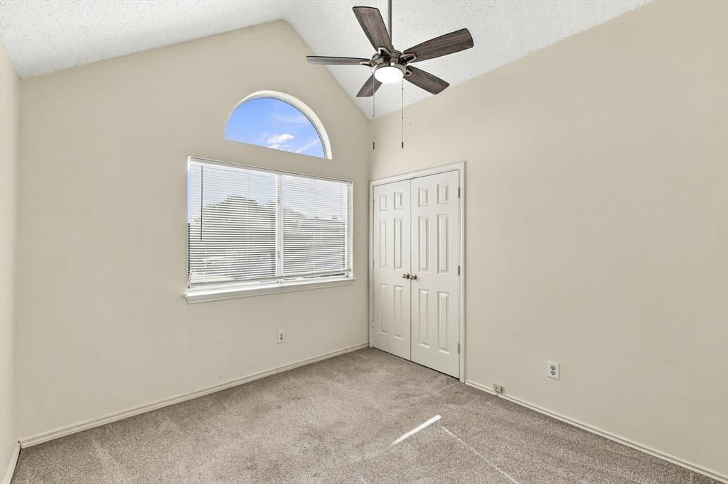 Vaulted ceiling, arched window, neutral wall-to-wall carpeting, ceiling fan with light fixture, and double-door closet
