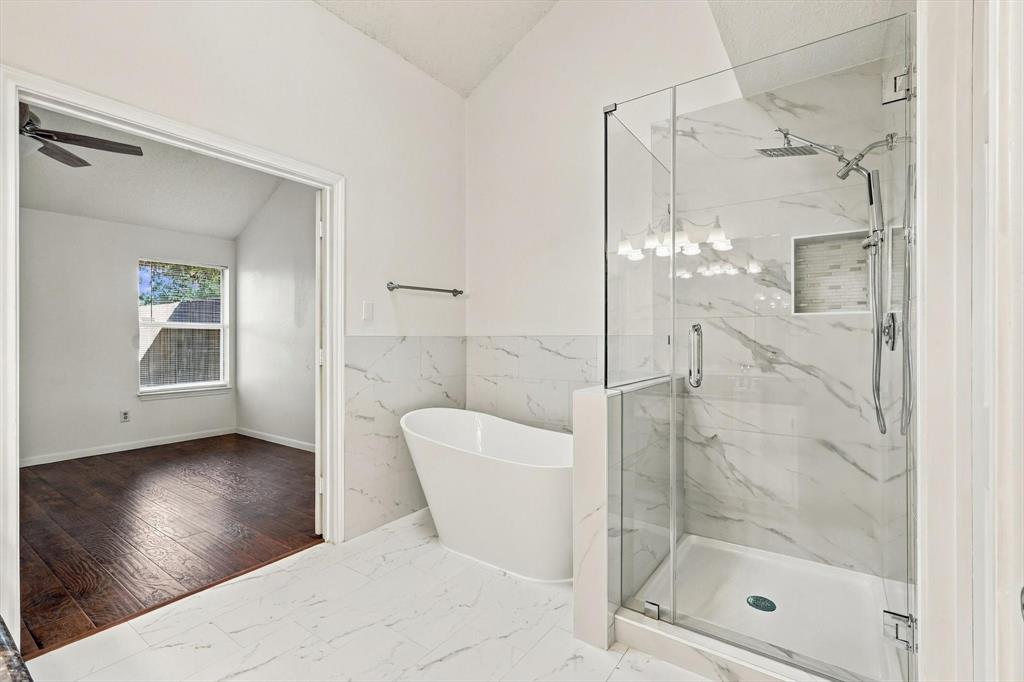 Freestanding soaking tub, walk-in shower with frameless glass enclosure, and wall-to-wall stone-finish tile detailing