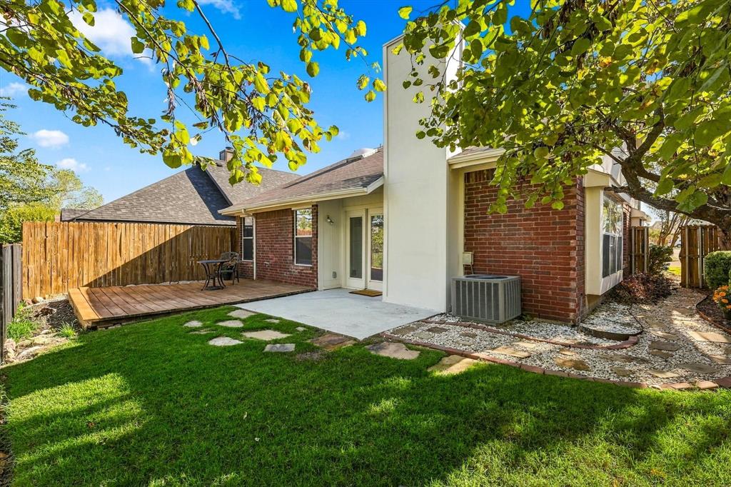 Backyard featuring brick exterior walls, a wood deck, a concrete patio, a central chimney, and stone-accented landscape pathways