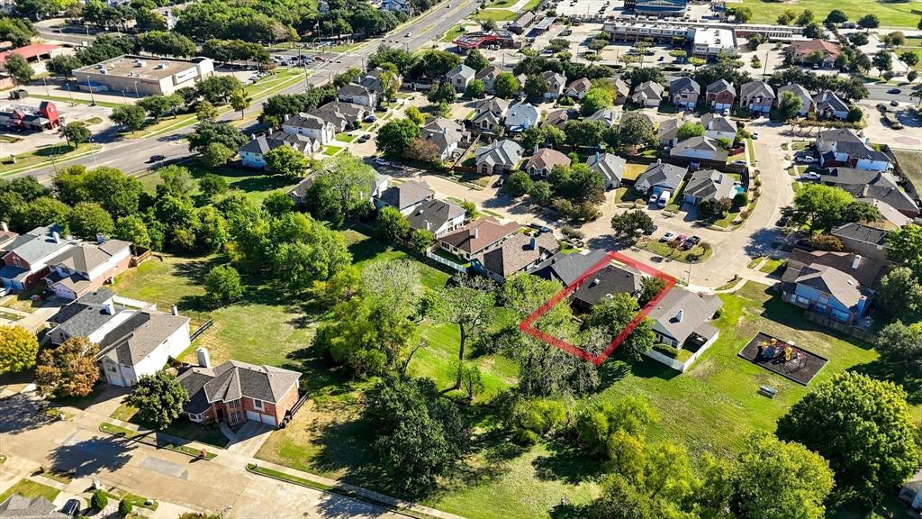 Aerial perspective of a residential property featuring a pitched composition shingle roof, expansive tree coverage, and an open grass lot