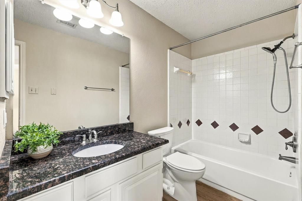 Bathroom featuring a stone-look countertop, undermount sink, multi-bulb vanity light, and a tiled shower-tub combination with an adjustable handheld showerhead