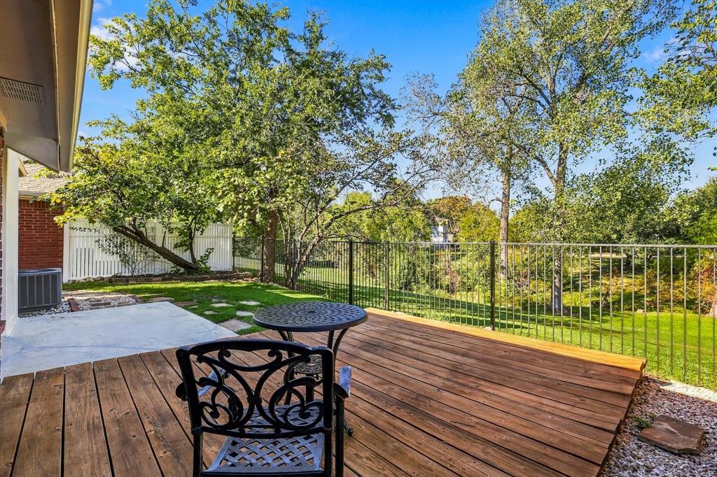 Wood deck, concrete patio, metal perimeter fencing, and mature trees