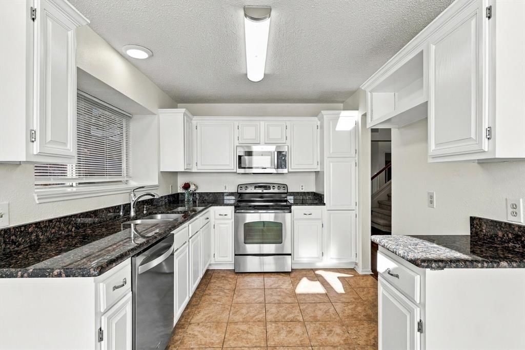 Kitchen featuring white shaker-style cabinetry, stone countertops, tile flooring, and stainless steel appliances including an over-the-range microwave