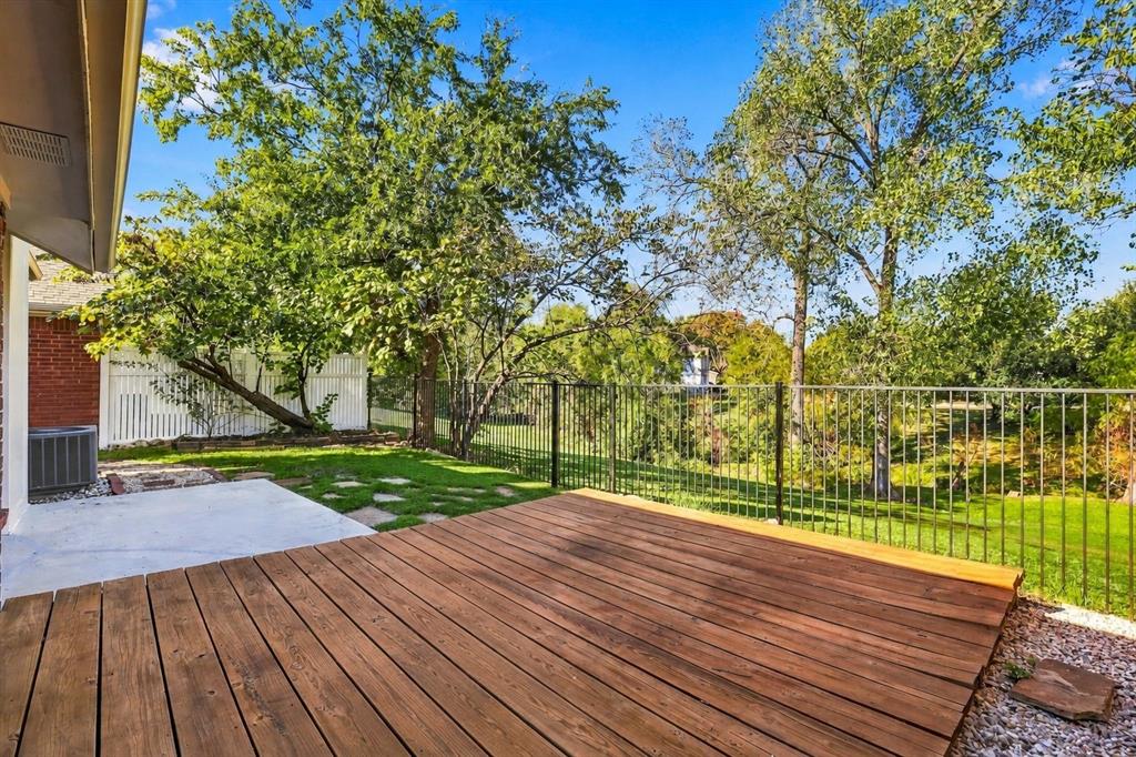 Backyard featuring a raised wooden deck, concrete patio area, black metal perimeter fencing, and mature trees