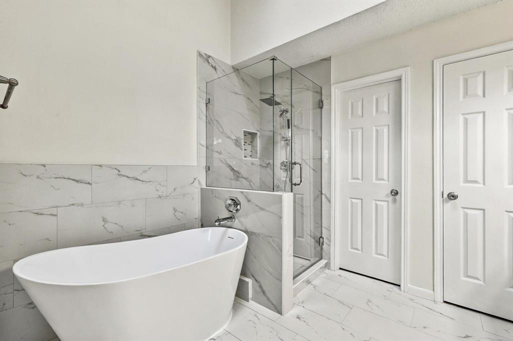 Freestanding soaking tub paired with a glass-enclosed shower featuring large-format tile surround, recessed wall niche, and integrated rainfall showerhead