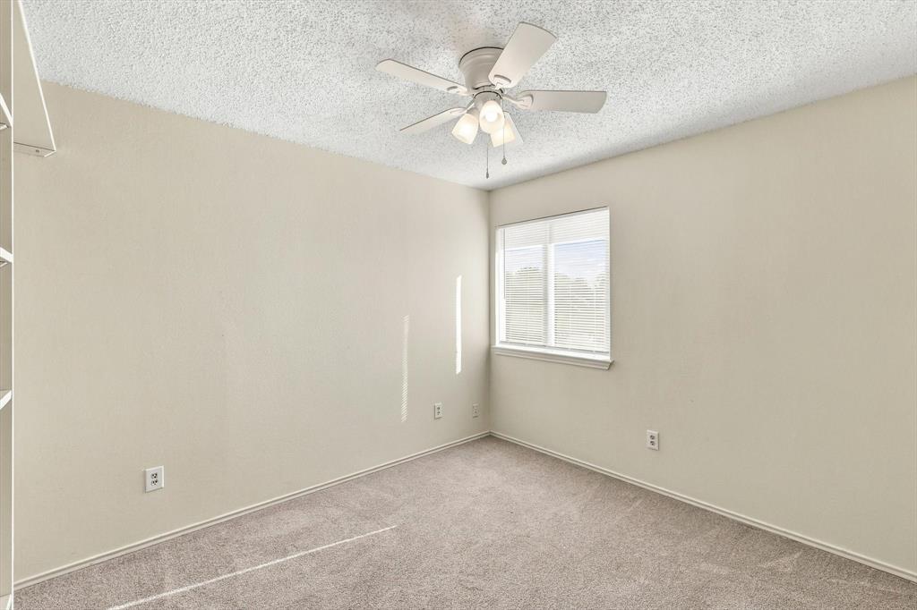 Neutral-toned interior space featuring carpeted flooring, textured ceiling, single window, and a multi-light ceiling fan