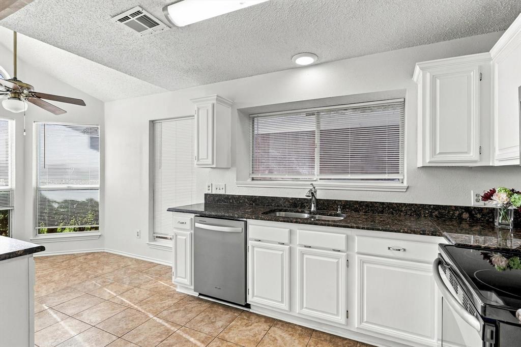 Kitchen featuring white shaker-style cabinetry, stone countertops, stainless steel dishwasher, tile flooring, and vaulted ceilings