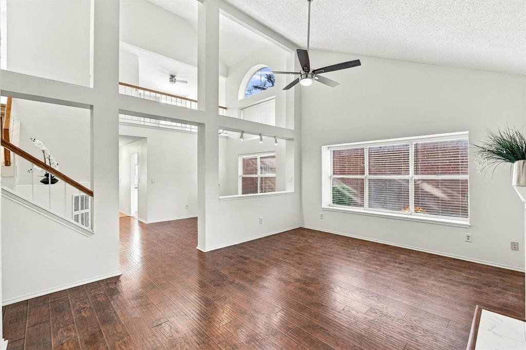 Vaulted ceilings, wood-finish flooring, multi-level interior windows, staircase with wooden handrail, and integrated ceiling fan with lighting
