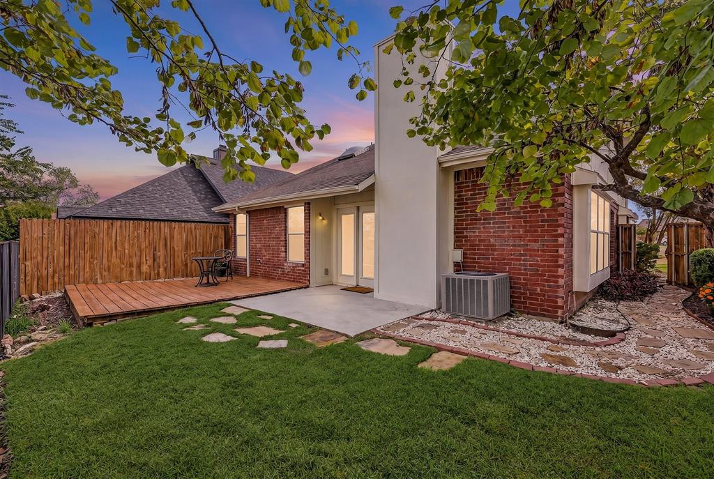 Exterior featuring brick masonry, a wood deck, concrete patio, natural stone hardscaping, and wood fencing