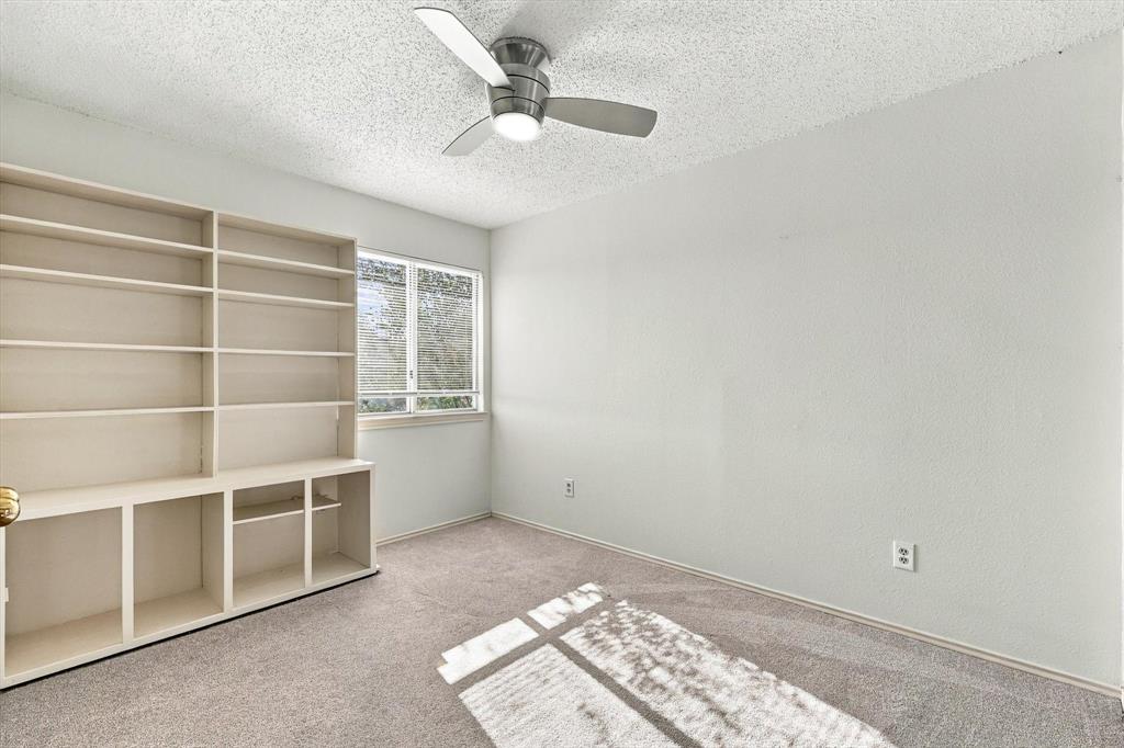 Room featuring built-in floor-to-ceiling shelving, neutral carpeting, a dual-pane window, and a ceiling fan with integrated lighting