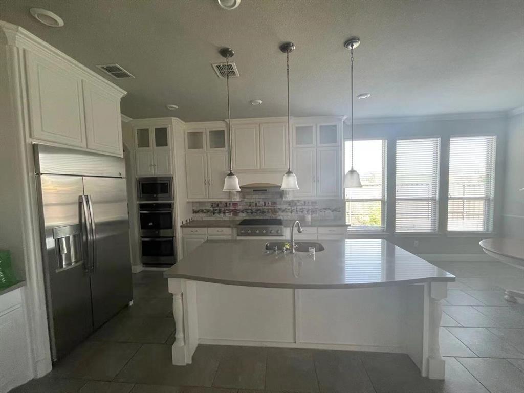 Kitchen featuring an oversized central island with solid-surface countertop, white cabinetry, stainless steel professional-grade refrigerator, built-in double wall ovens, and recessed lighting