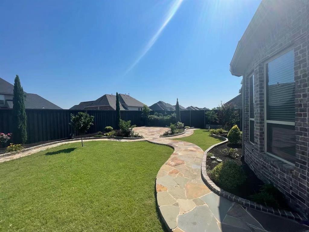 Backyard featuring a flagstone patio, winding flagstone walkway, manicured lawn, established landscaping, and perimeter privacy fencing