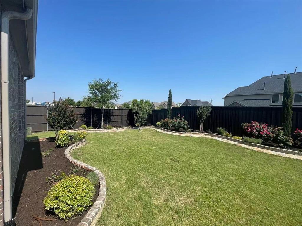 Backyard featuring a manicured lawn, stone-bordered garden beds, dark wood-style perimeter fencing, and mature ornamental shrubs