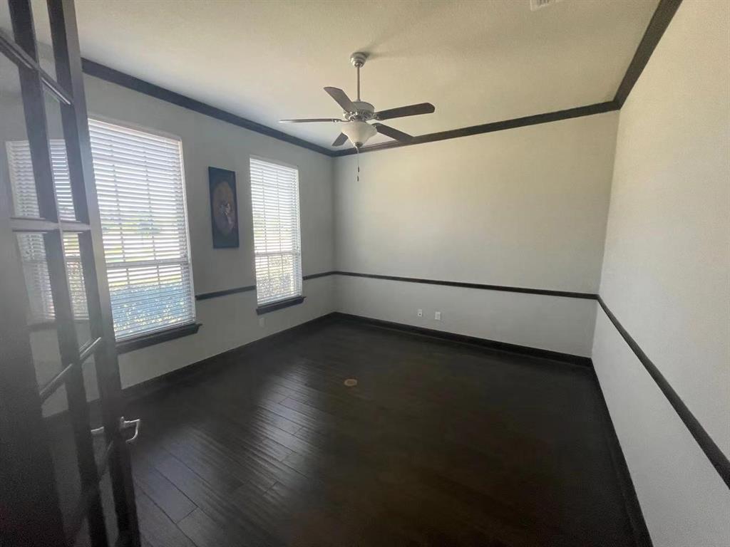 Room featuring wood-finish flooring, dark-toned crown and chair rail molding, dual-pane windows, and a ceiling fan with integrated lighting