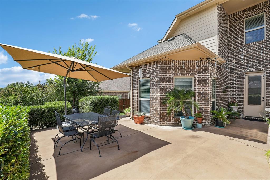 Concrete patio featuring multi-toned brick masonry, fiber-cement siding, a prominent bay-style architectural element, and mature hedge landscaping