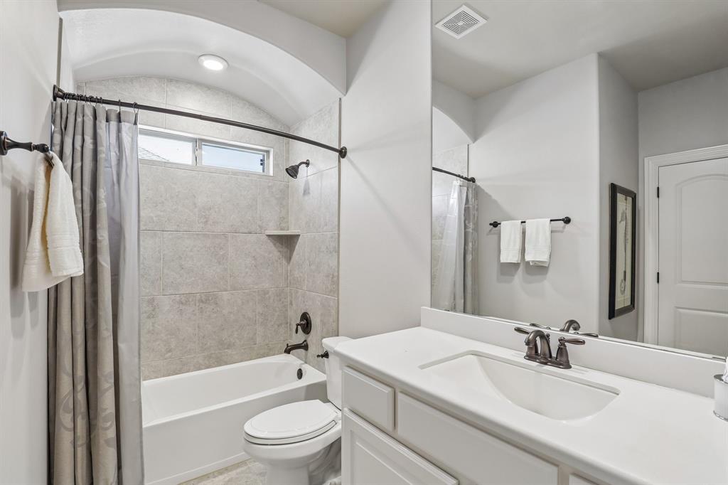 Bathroom featuring a tub-shower combination with floor-to-ceiling tile surround, arched ceiling, white cabinetry with a solid-surface countertop, and oil-rubbed bronze fixtures