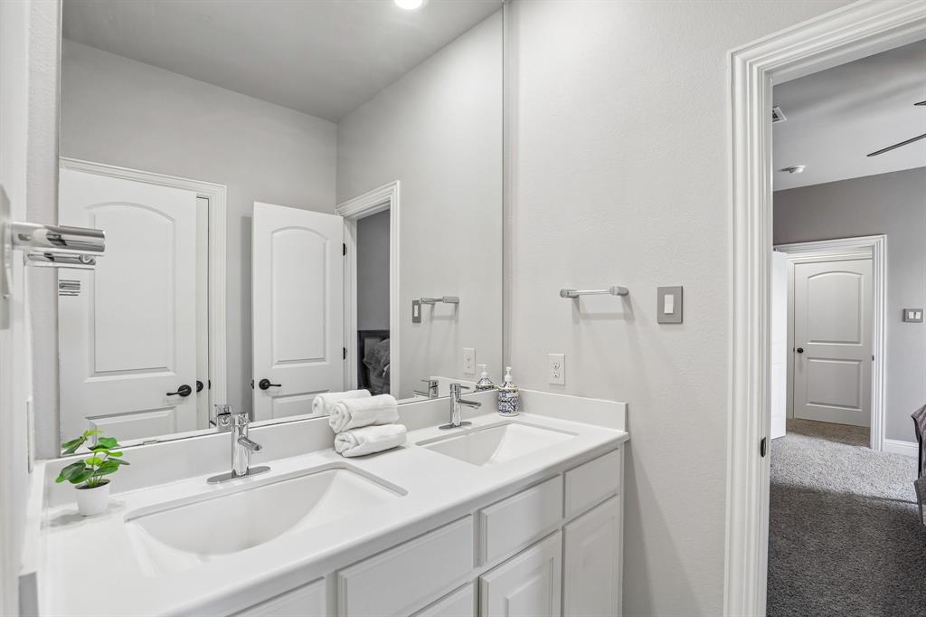 Dual-sink vanity with a solid-surface countertop, full-width wall mirror, chrome fixtures, and white shaker-style cabinetry
