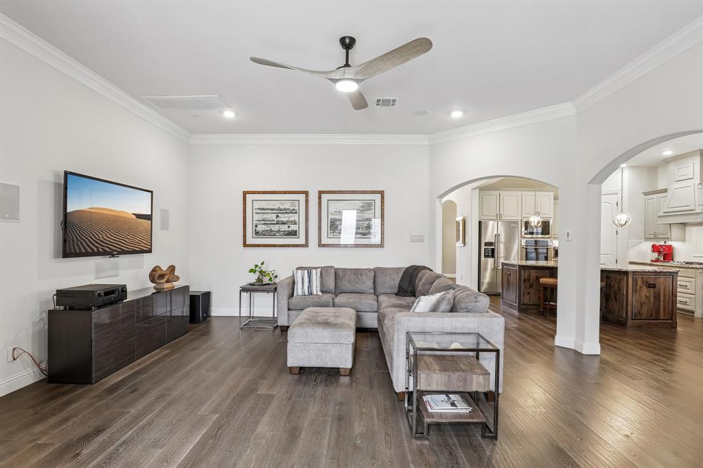 Living area featuring wood-finish flooring, crown molding, a central ceiling fan with integrated lighting, and an arched entry