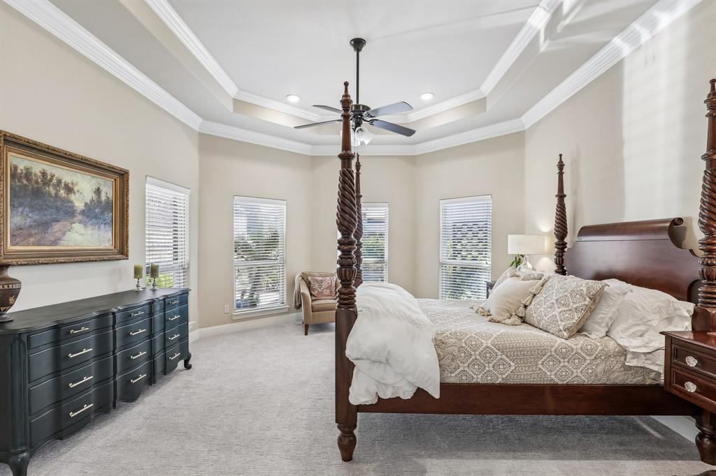 Large primary bedroom with tray ceiling with crown molding, recessed lighting, central ceiling fan, and multiple windows