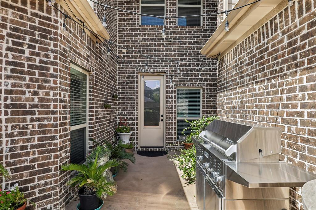 Exterior brick courtyard featuring a concrete patio, built-in stainless steel grill, and string lighting
