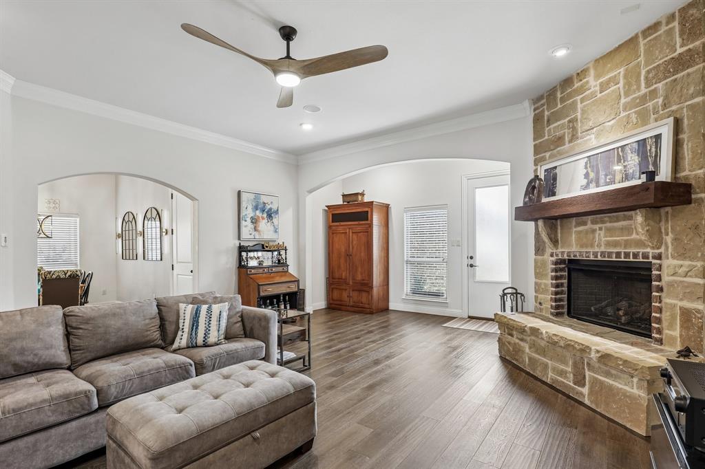 Living area featuring floor-to-ceiling stone masonry fireplace with wooden mantel, wood-finish flooring, vaulted ceiling with integrated blade-style ceiling fan, and arched architectural entryways