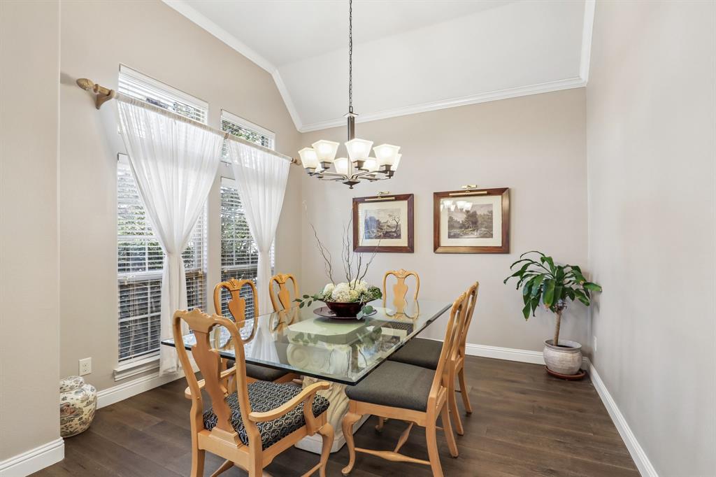 Large dining room with vaulted ceiling with crown molding, wood-finish flooring, multi-pane windows, and a tiered chandelier Large dining room with vaulted ceiling with crown molding, wood-finish flooring, multi-pane windows, and a tiered chandelier
