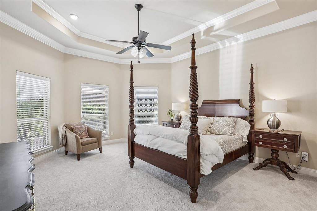 Large primary bedroom with tray ceiling with crown molding, ceiling fan with integrated lighting, and multiple windows with horizontal blinds