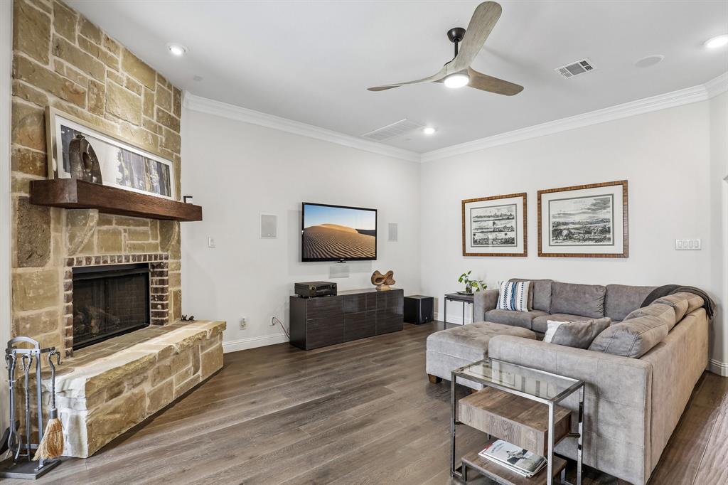 Living area featuring a floor-to-ceiling stone fireplace, heavy timber mantel, wood-finish flooring, crown molding, and a modern ceiling fan