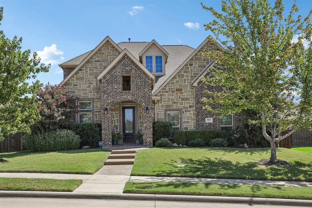 Multi-gabled exterior facade featuring stone veneer and brick accents, decorative arched entryway, and concrete walkway