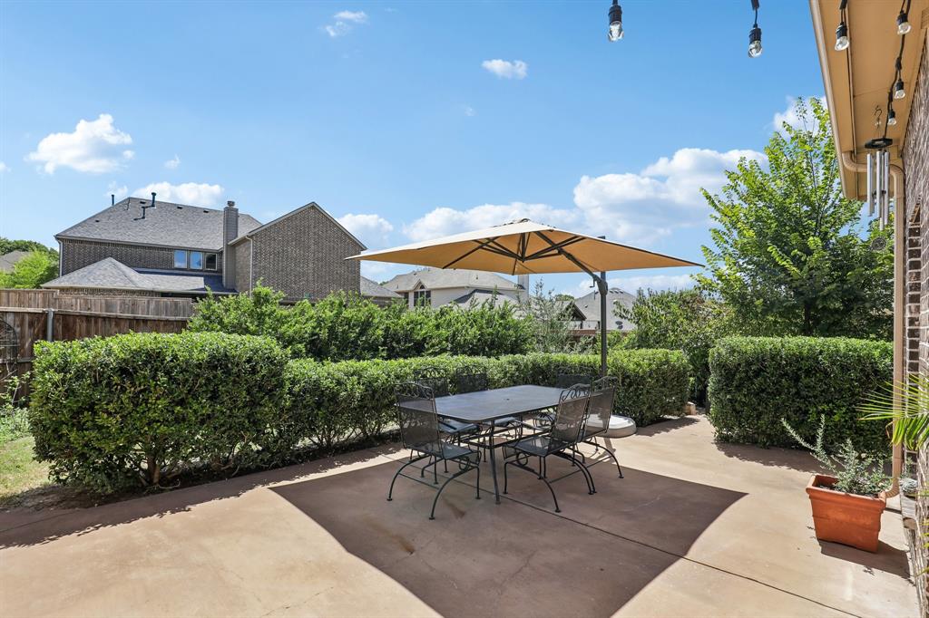 Concrete patio featuring brick exterior wall, mature privacy hedging, and overhead string lighting