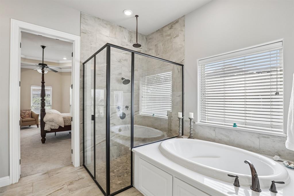 Walk-in shower with matte black frame, large-format tile surround, rainfall showerhead, built-in soaking tub with deck-mount faucet, and wood-finish tile flooring in the primary bathroom